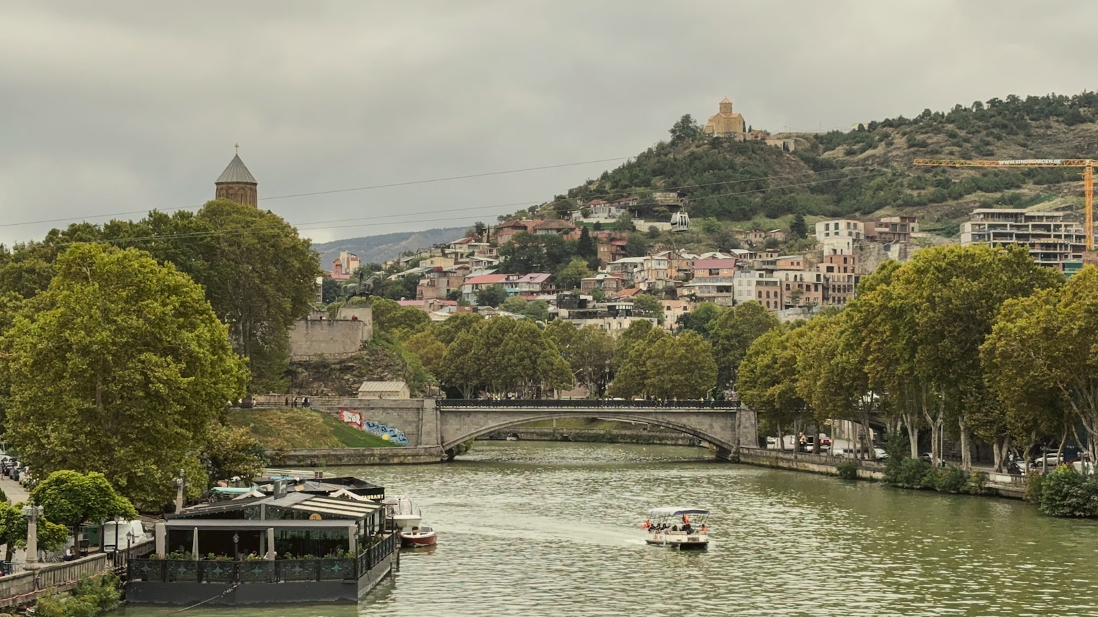 The Kura River and a stone bridge in Tbilisi, with the hillside old town and a hilltop church behind