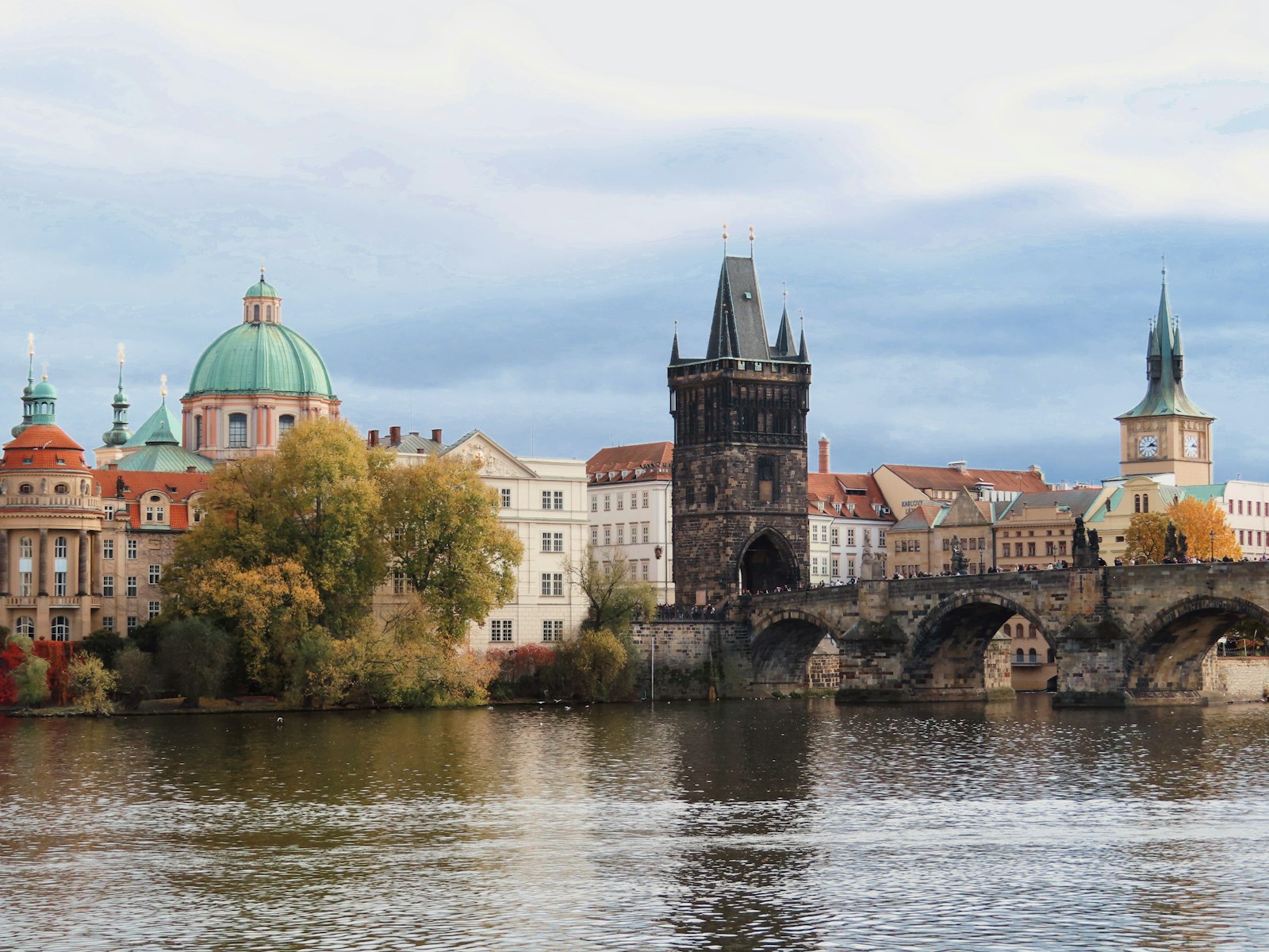 Charles Bridge and the Old Town Bridge Tower across the Vltava River in Prague, with green church domes behind