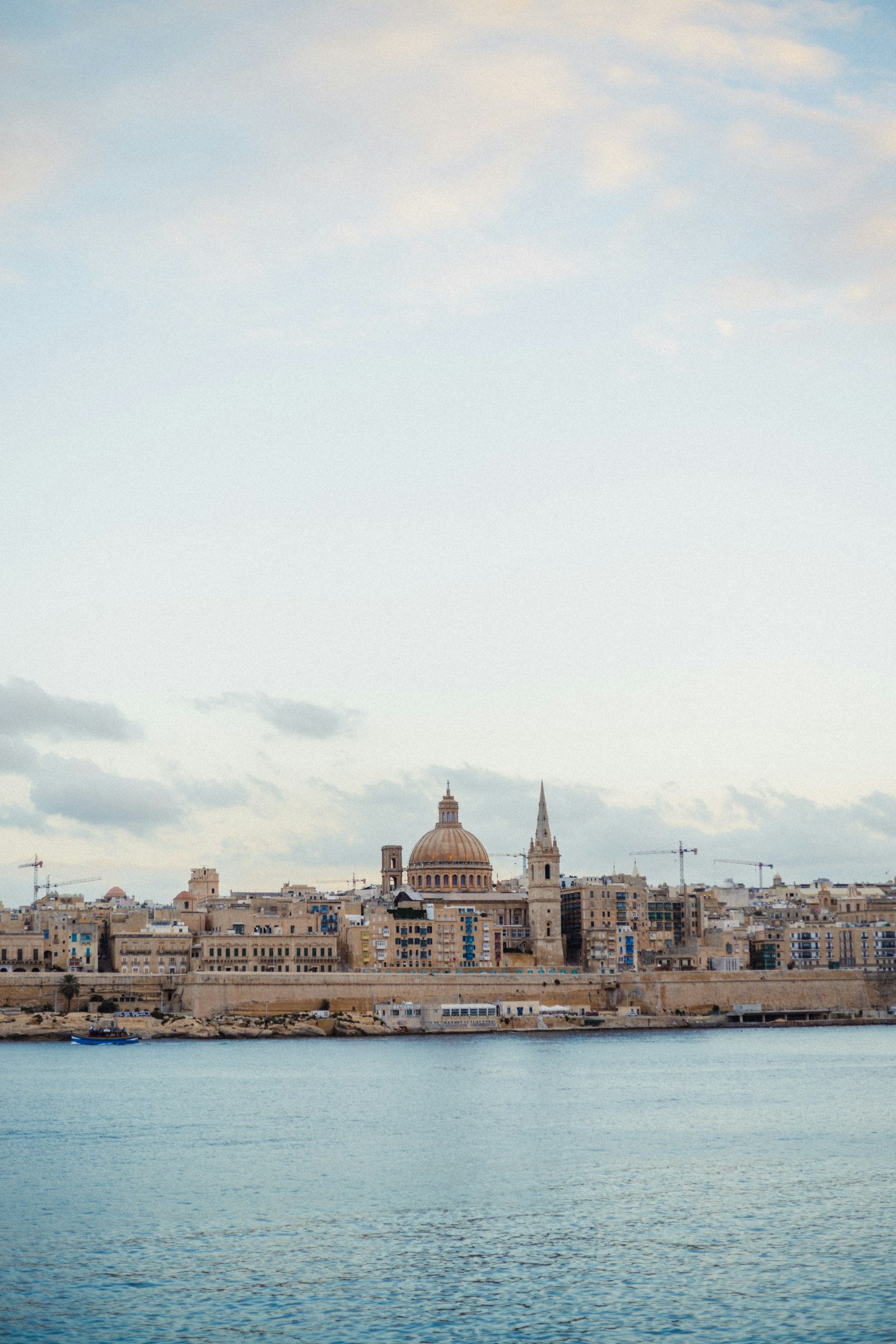Valletta's skyline across the harbour, with the dome of the Carmelite Church and a church spire rising above the sandstone city walls